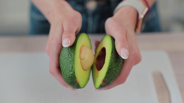 Close-up of a woman holding half of fresh ripe avocado in hand, top view.